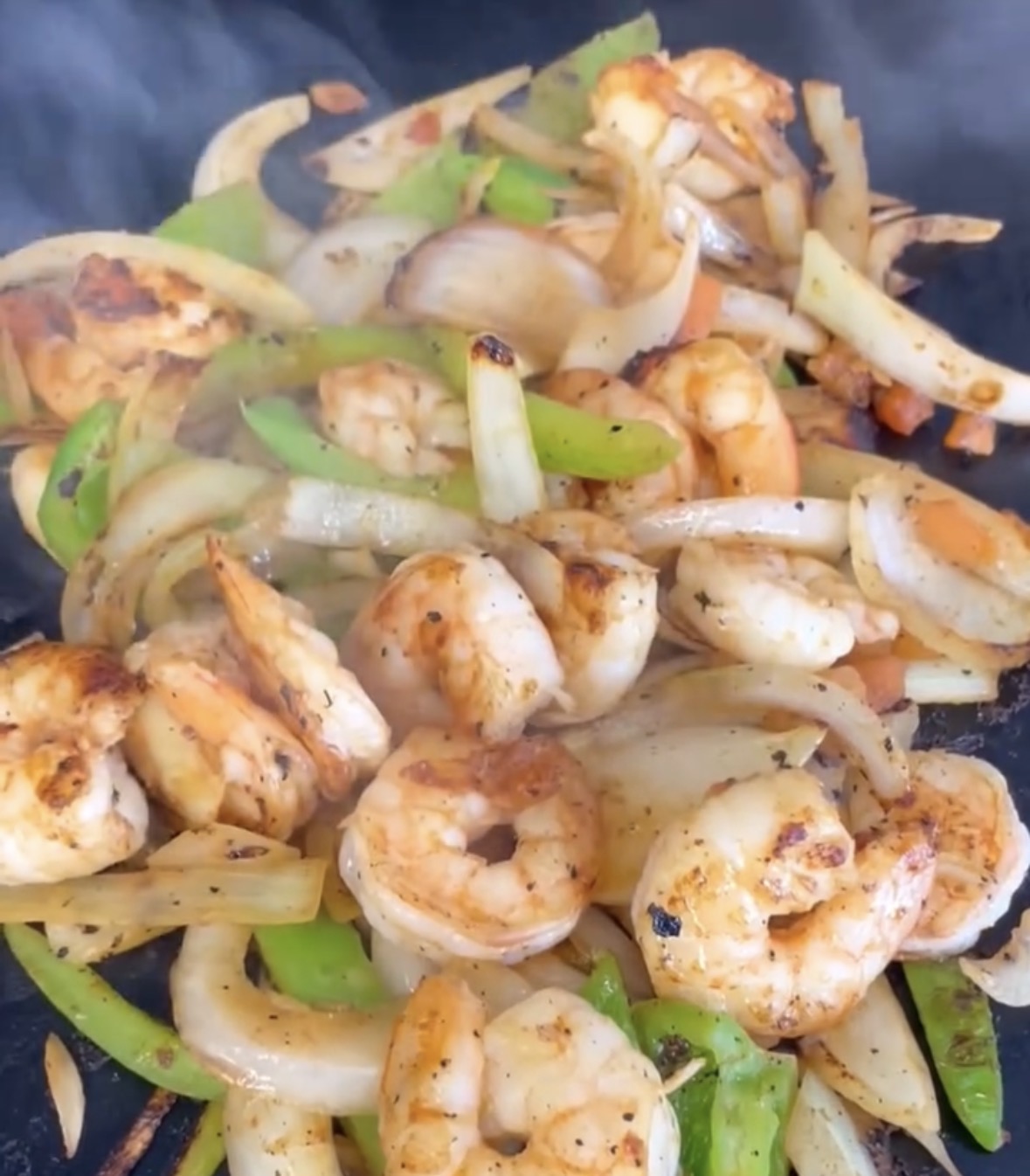Shrimp fajitas sizzling with peppers and onions on the griddle